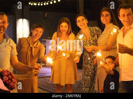 Gruppo di ospiti di nozze che tengono accese luci bengala all'aperto durante il cocktail party di nozze. Concetto di felicità, gioia e celebrazione Foto Stock