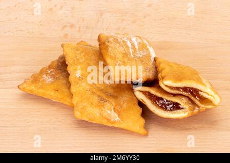 Bugie (bugie) o frappe o chiacchiere o angelo wings.Traditional italiano carnevale fritto dessert riempito con marmellata d'arancia, isolato su tavola di legno Foto Stock