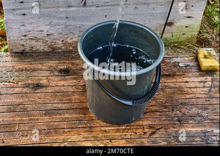 un secchio di plastica nera è riempito di acqua dalla pompa Foto Stock