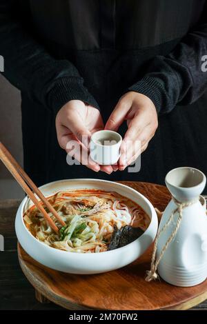 Composizione sake giapponese con zuppa asiatica con spaghetti di riso, cerimonia del pasto asiatico con fiori di magnolia Foto Stock