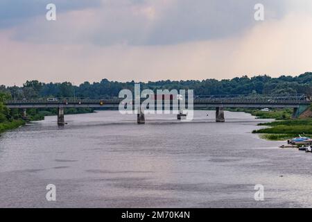 Ponte sul fiume tra alberi verdi in una giornata nuvolosa estiva. Fiume. Foto Stock