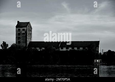 Una vecchia fabbrica abbandonata su una riva del fiume Foto Stock