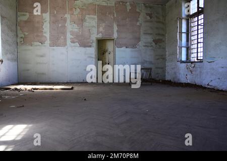 Una stanza in un edificio abbandonato con una sedia rotta in esso. Foto Stock