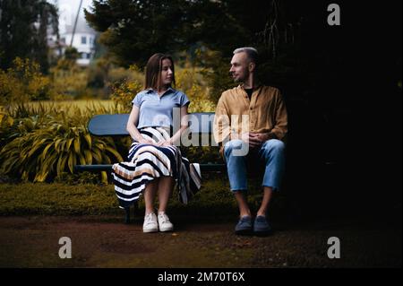 Una foto romantica di una giovane coppia seduta su una panchina in un bellissimo parco autunnale, guardandosi con amore e affetto Foto Stock