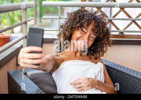 Felice donna brasiliana con vitiligo prendendo selfie al centro benessere, Wellness momento dopo trattamenti di bellezza Foto Stock
