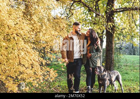 giovane coppia a piedi con il cane in un parco, scenario autunnale, lifestyle felice dei giovani amanti e concetto di animale domestico Foto Stock