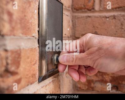 Campanello che suona con il pollice. Primo piano di mano maschile spingendo a casa citofono porta pulsante campana. Foto Stock