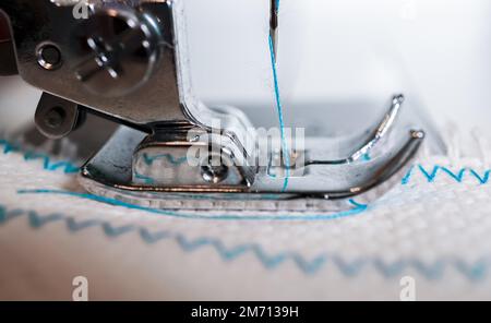 Primo piano dell'ago della macchina da cucire con filo blu cucito su un tessuto bianco Foto Stock