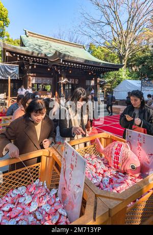 saitama, kawagoe - dic 31 2021: Turisti asiatici femmine in possesso di una canna da pesca cattura fortuna diving carte a forma di snapper rosso chiamato Aitai mikuji per Foto Stock