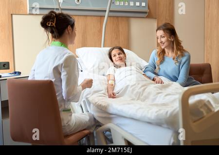 Giovane paziente, sua madre e il medico femminile comunicano nella stanza dell'ospedale Foto Stock