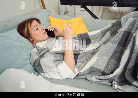 Donna malata chiamata sul cellulare in camera da letto Foto Stock