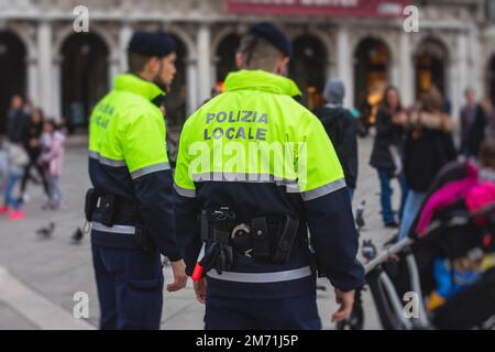 Formazione di pattuglia della polizia italiana vista posteriore con logo 'polizia locale' emblema su uniforme mantenere l'ordine pubblico nelle strade di Venezia, Venezia, IT Foto Stock