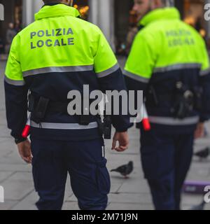 Formazione di pattuglia della polizia italiana vista posteriore con logo 'polizia locale' emblema su uniforme mantenere l'ordine pubblico nelle strade di Venezia, Venezia, IT Foto Stock