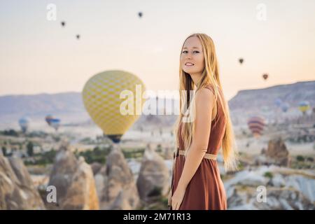 Donna turistica che guarda mongolfiere in Cappadocia, Turchia. Buon viaggio in Turchia concetto. Donna in cima a una montagna che gode di una vista meravigliosa Foto Stock
