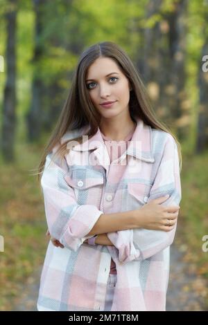 Donna bionda in abito casual a piedi lungo autunno tiglio albero vicolo. Percorso sotto gli alberi gialli con foglie autunnali in caduta. Giorno autunnale soleggiato. T Foto Stock