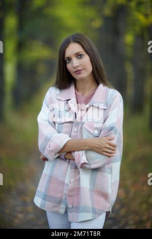 Donna bionda in abito casual a piedi lungo autunno tiglio albero vicolo. Percorso sotto gli alberi gialli con foglie autunnali in caduta. Giorno autunnale soleggiato. T Foto Stock