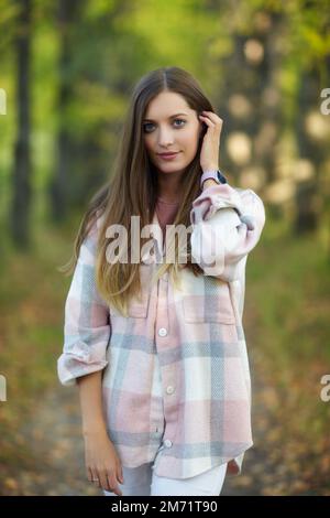 Donna bionda in abito casual a piedi lungo autunno tiglio albero vicolo. Percorso sotto gli alberi gialli con foglie autunnali in caduta. Giorno autunnale soleggiato. T Foto Stock