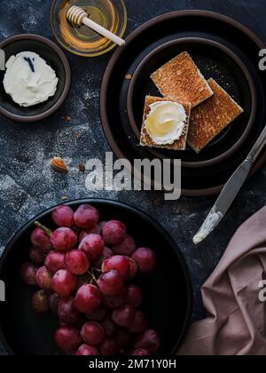 L'uva e il formaggio cremoso brinda con miele su piatti neri Foto Stock