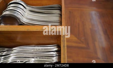 Posate a cucchiaio in acciaio inossidabile cromato disposte in modo ordinato in un contenitore di legno Foto Stock