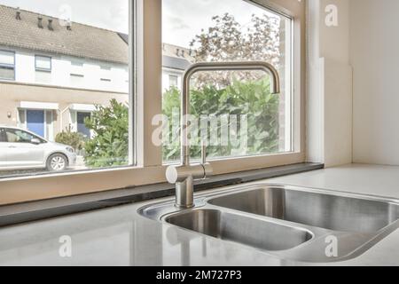 un lavello da cucina davanti ad una finestra con vista sulla strada e gli alberi all'esterno, presi dall'interno Foto Stock