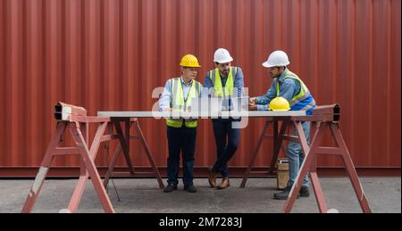 Addetto alla spedizione che indica il programma di spedizione sul tablet, spiega al collega la pianificazione della spedizione successiva. Un contenitore grande è in th Foto Stock