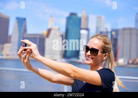 Godetevi le attrazioni della città. una giovane donna attraente che scatta una foto mentre si trova accanto ad un fiume in una città. Foto Stock