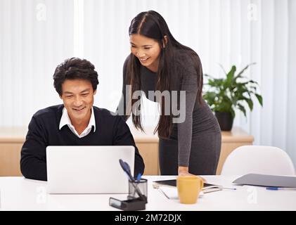 Due menti sono meglio di una. due colleghi aziendali che lavorano insieme in un computer portatile in ufficio. Foto Stock