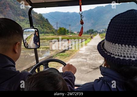 Una madre di minoranza etnica tailandese bianca siede accanto a suo figlio mentre guida un'auto elettrica turistica a mai Chau, negli altopiani del Vietnam settentrionale. Foto Stock