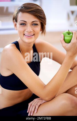 Mangiare bene e mantenersi in forma. una giovane donna sportiva seduta sul pavimento di una palestra che mangia una mela. Foto Stock