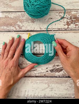 Una vista dall'alto delle mani di una donna con chiodi dipinti che tessono una palla di filo verde Foto Stock