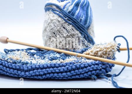 Macro vista della matassa di filato blu e bianco e di un tessuto lavorato a maglia con una combinazione di texture lisce e ruvide, su sfondo bianco Foto Stock