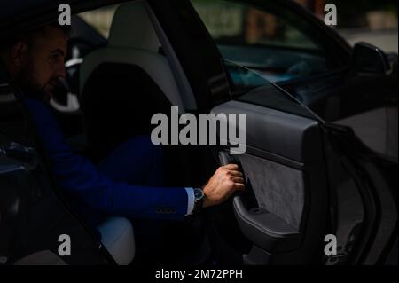 Un uomo in tuta blu apre la porta dell'auto. Primo piano della mano di un uomo con un orologio costoso. Foto Stock