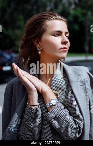 Verticale trendy sicuro attraente, donna d'affari bionda alla moda in giacca grigia guardare lontano con le mani si piegano insieme Foto Stock