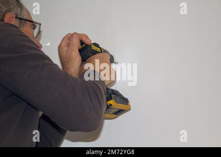 Immagine di un uomo che perfora i fori in una parete della casa con un trapano. Montaggio di un ripiano a parete. Fatelo voi stessi lavori. Foto Stock