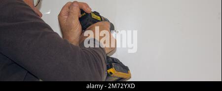 Immagine di un uomo che perfora i fori in una parete della casa con un trapano. Montaggio di un ripiano a parete. Fatelo voi stessi lavori. Banner orizzontale Foto Stock