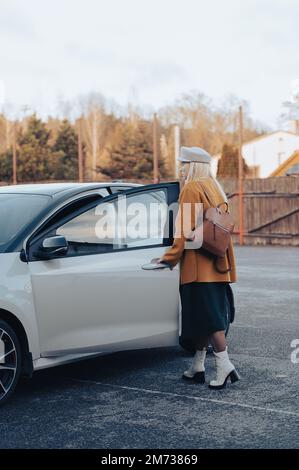 Elegante donna d'affari di mezza età in piedi alla macchina, moda autunnale, autencic full body ritratto Foto Stock