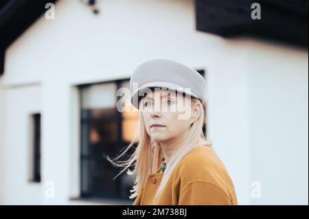 Primo piano volto ritratto europeo donna di mezza età con occhi verdi blu in cappello moda autunno Foto Stock