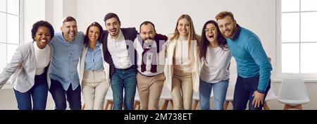 Team multietnico di giovani uomini d'affari felici che abbraccia e ride tutti insieme Foto Stock