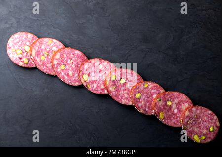Fila di fette di salsiccia di salame su una tavola nera. Sfondo scuro Foto Stock