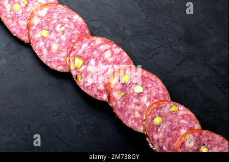 Fila di fette di salsiccia di salame su una tavola nera. Sfondo scuro Foto Stock
