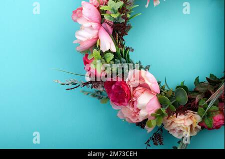 Corona di fiori artificiali colorati isolato su sfondo verde acqua chiaro Foto Stock