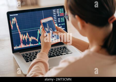 Donna crypto trader investitore broker utilizzando smartphone app e laptop esecuzione finanziaria borsa trading ordine di mercato per acquistare o vendere criptovaluta. Messa a fuoco selettiva sulle mani e sullo schermo del cellulare Foto Stock