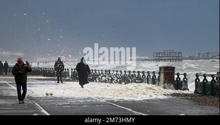 Brighton UK 7th Gennaio 2023 - Walkers guado attraverso la schiuma di mare lungo il lungomare di Hove come tempeste battere la costa meridionale oggi con forti venti e pioggia : Credit Simon Dack / Alamy Live News Foto Stock