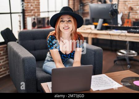 Giovane musicista caucasica sorridente sicuro di usare il portatile in studio musicale Foto Stock