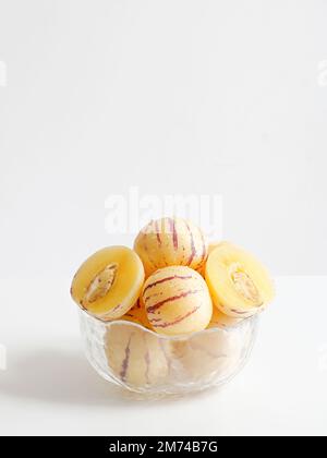 Uno shot verticale di meloni di pepino freschi in una ciotola di vetro su un tavolo bianco Foto Stock