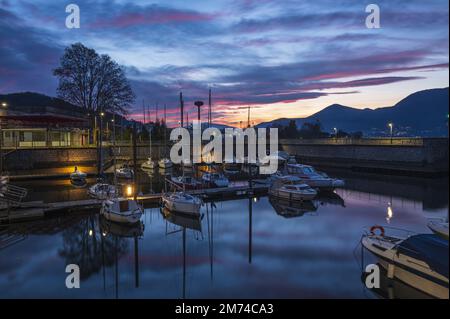 Bellissimo tramonto con nuvole colorate e barche che si riflettono nell'acqua del porto di Luino Foto Stock