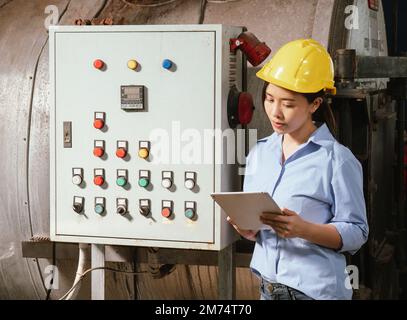 Lavoratrice di fabbrica che utilizza un computer tablet per controllare il funzionamento della macchina in una linea di produzione di fabbrica di bevande. Foto Stock