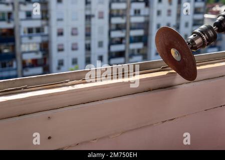 Levigare un vecchio telaio della finestra durante i lavori di ristrutturazione con un edificio di appartamenti sullo sfondo Foto Stock