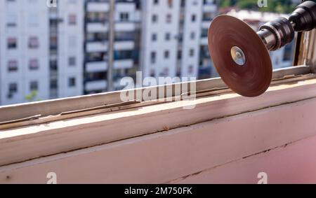 Levigare un vecchio telaio della finestra durante i lavori di ristrutturazione con un edificio di appartamenti sullo sfondo Foto Stock