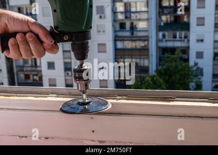 Levigare un vecchio telaio della finestra durante i lavori di ristrutturazione con un edificio di appartamenti sullo sfondo Foto Stock